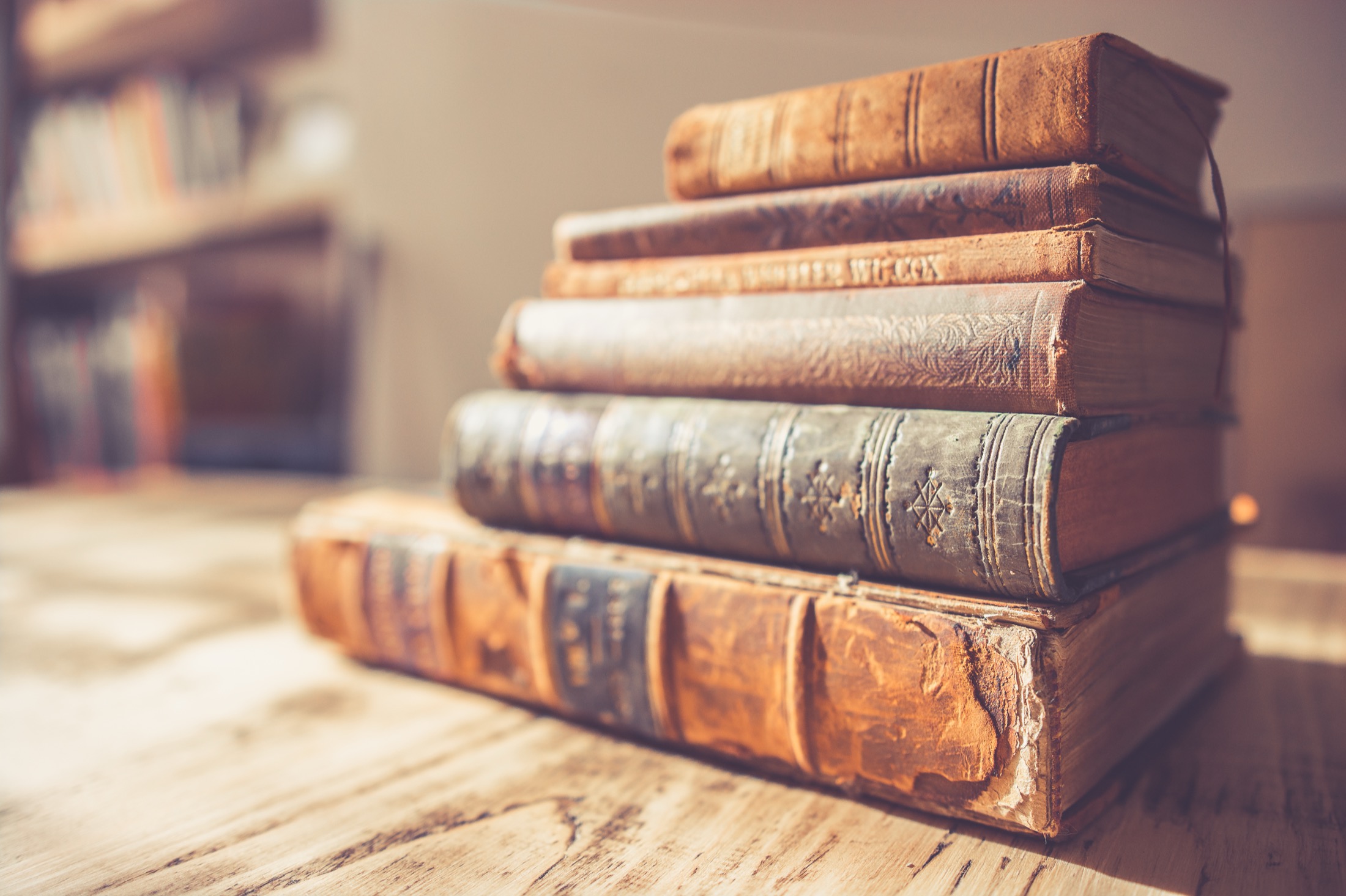 A stack of old leather-bound books on a sunlit wooden table